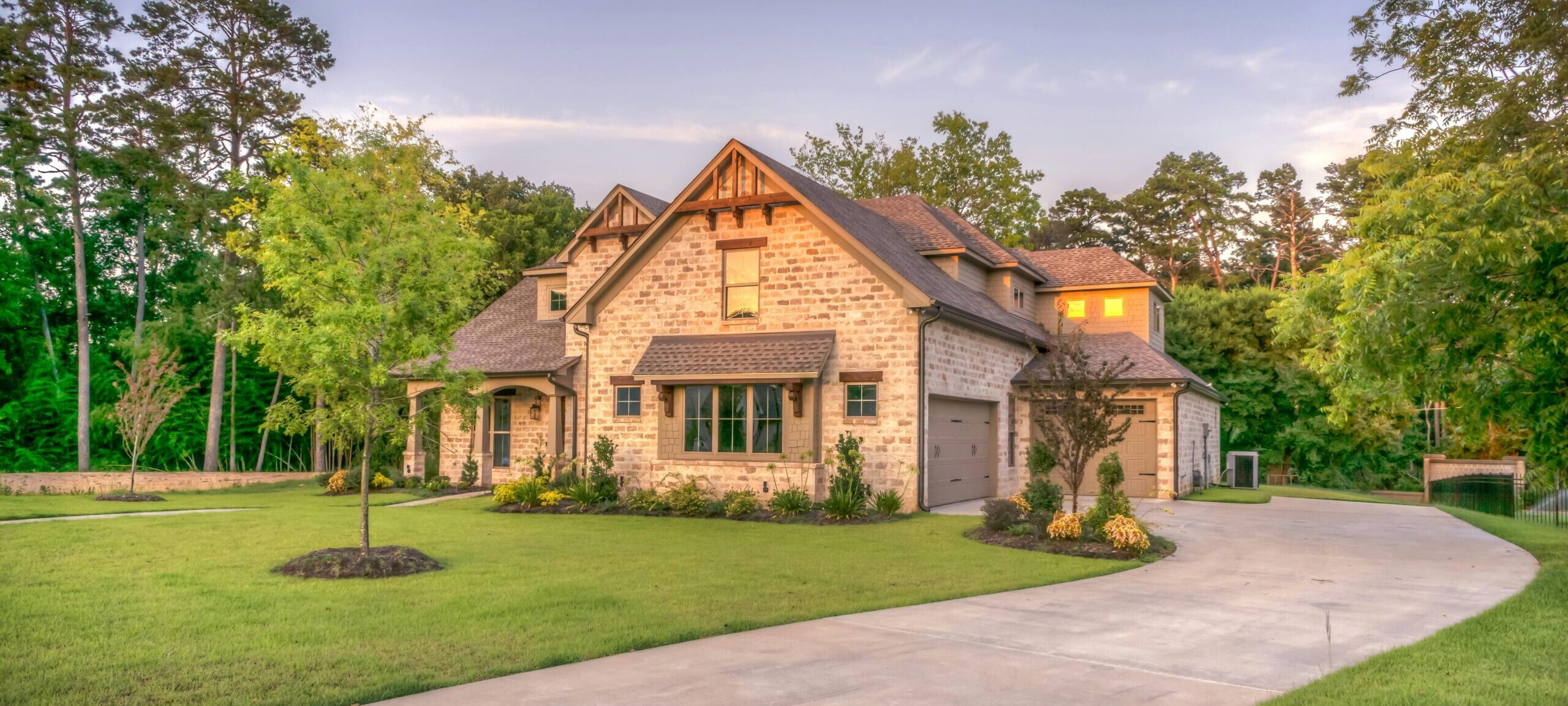 Elegant stone family home surrounded by trees, lush lawn, and vibrant garden.